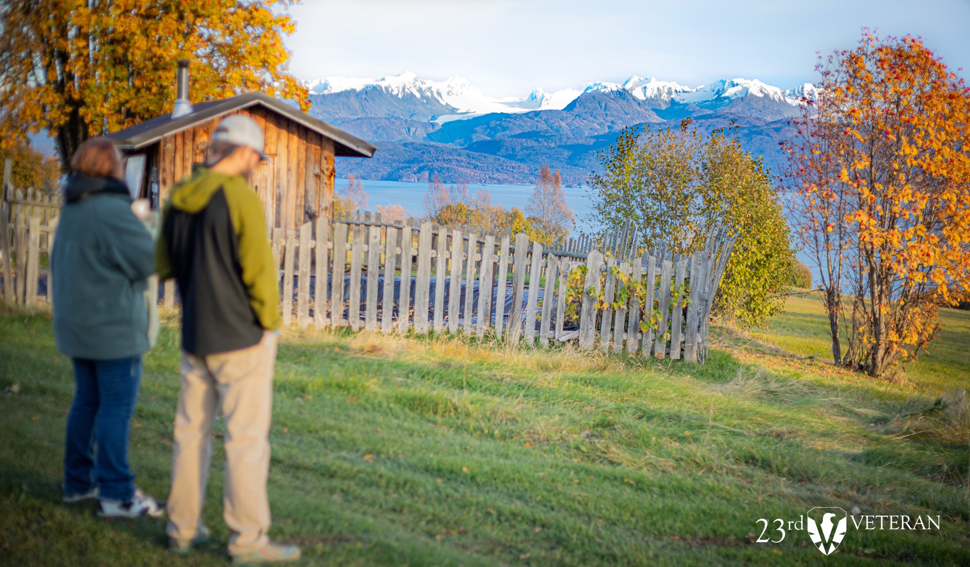 Two people walking toward a homestead overlooking Kachemak Bay and the mountains